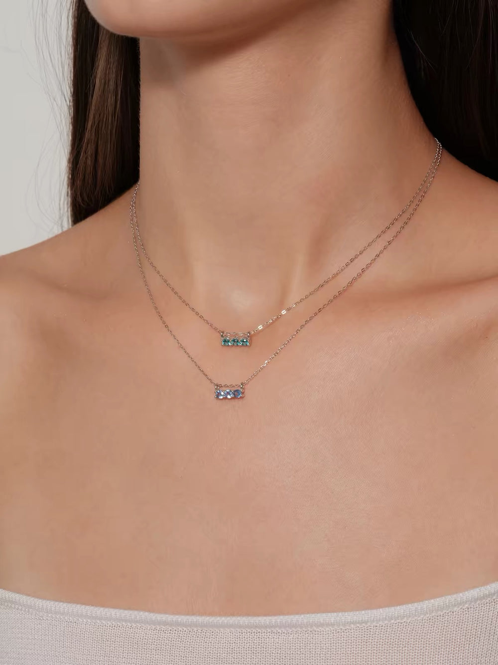 Model wearing layered blue and aqua three-stone necklaces